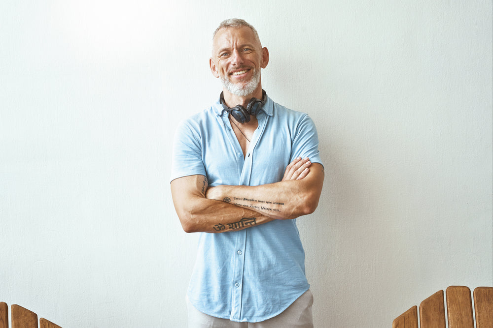 Portrait of a happy middle aged caucasian man keeping arms crossed and smiling at camera while standing against white wall