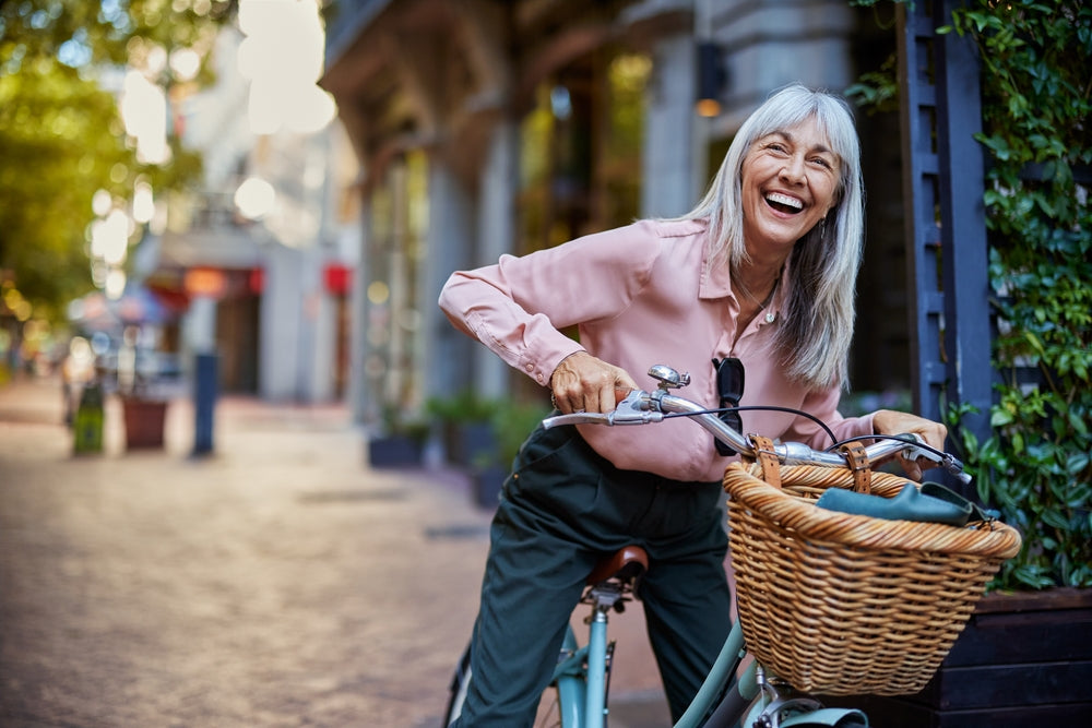 Portrait of happy middle aged woman laughing while holding her bicycle in a city street.